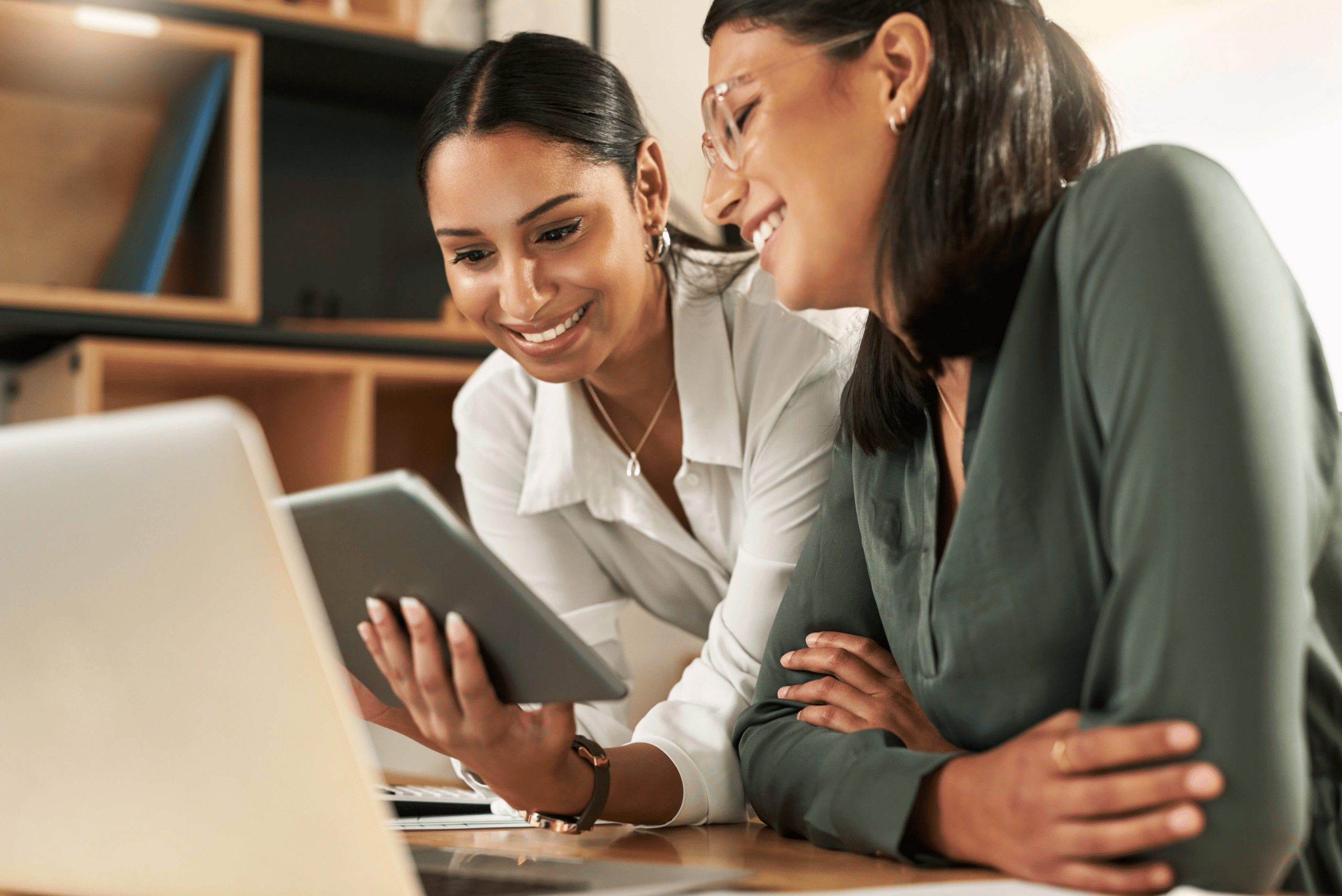 two women smiling and looking at a tablet