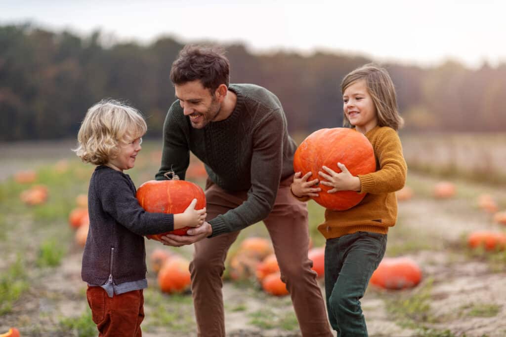 man handing pumpkins to two kids in a pumpkin patch