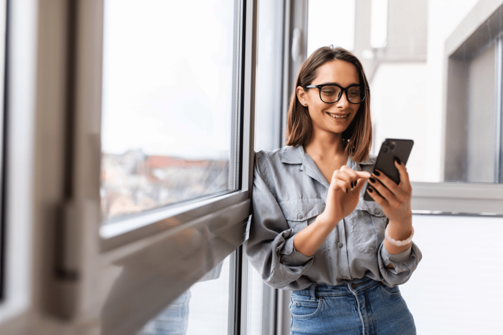 woman in glasses smiling at her mobile phone