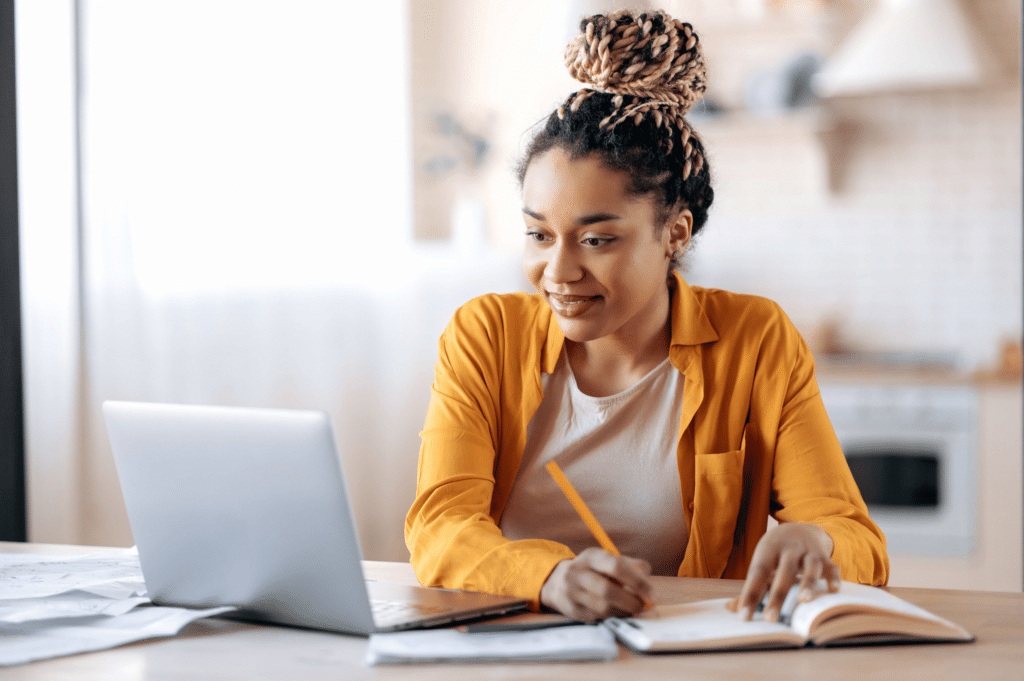 a woman taking notes on paper from her laptop